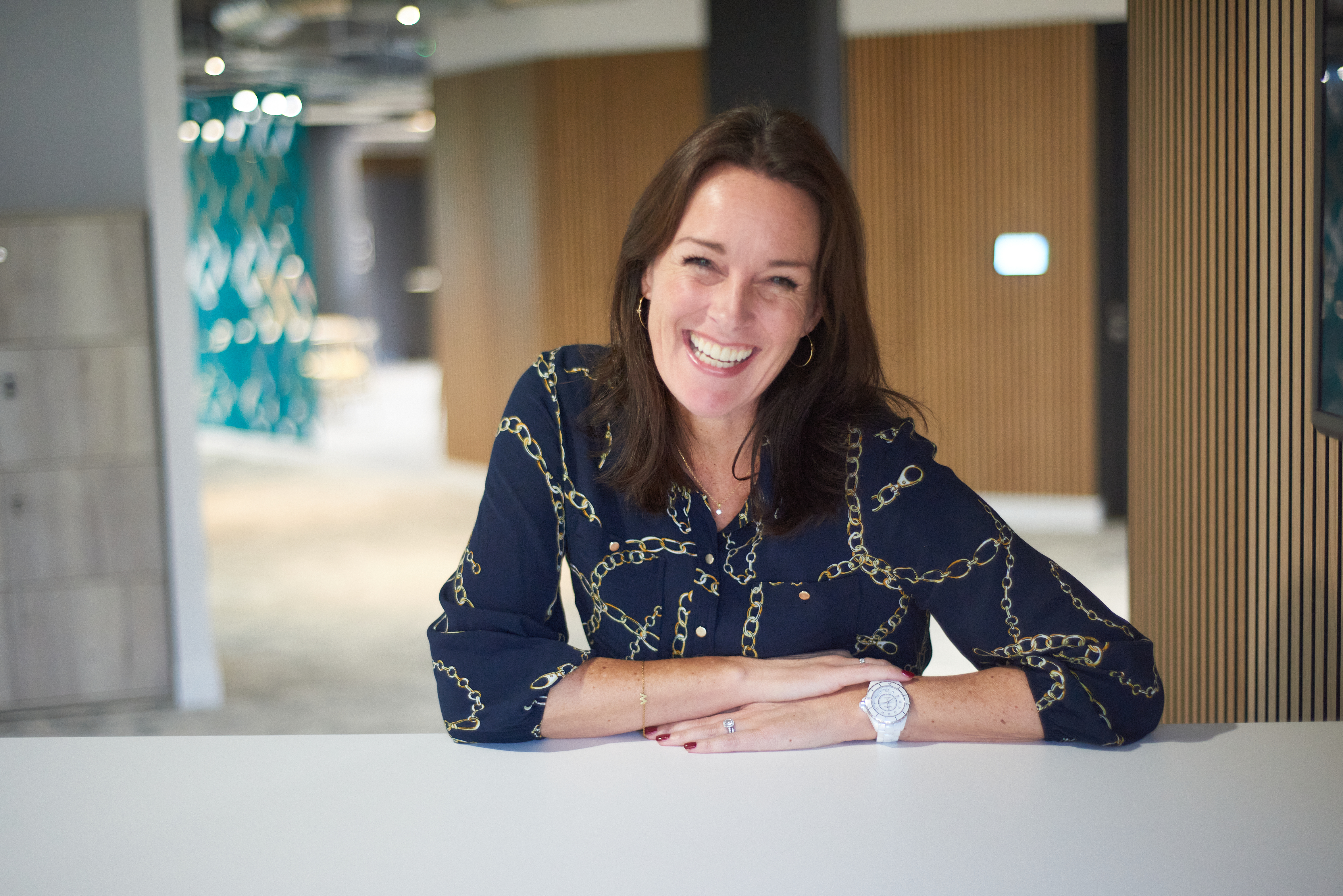 Wendy Shearer sitting at an office desk wearing a patterned navy blouse